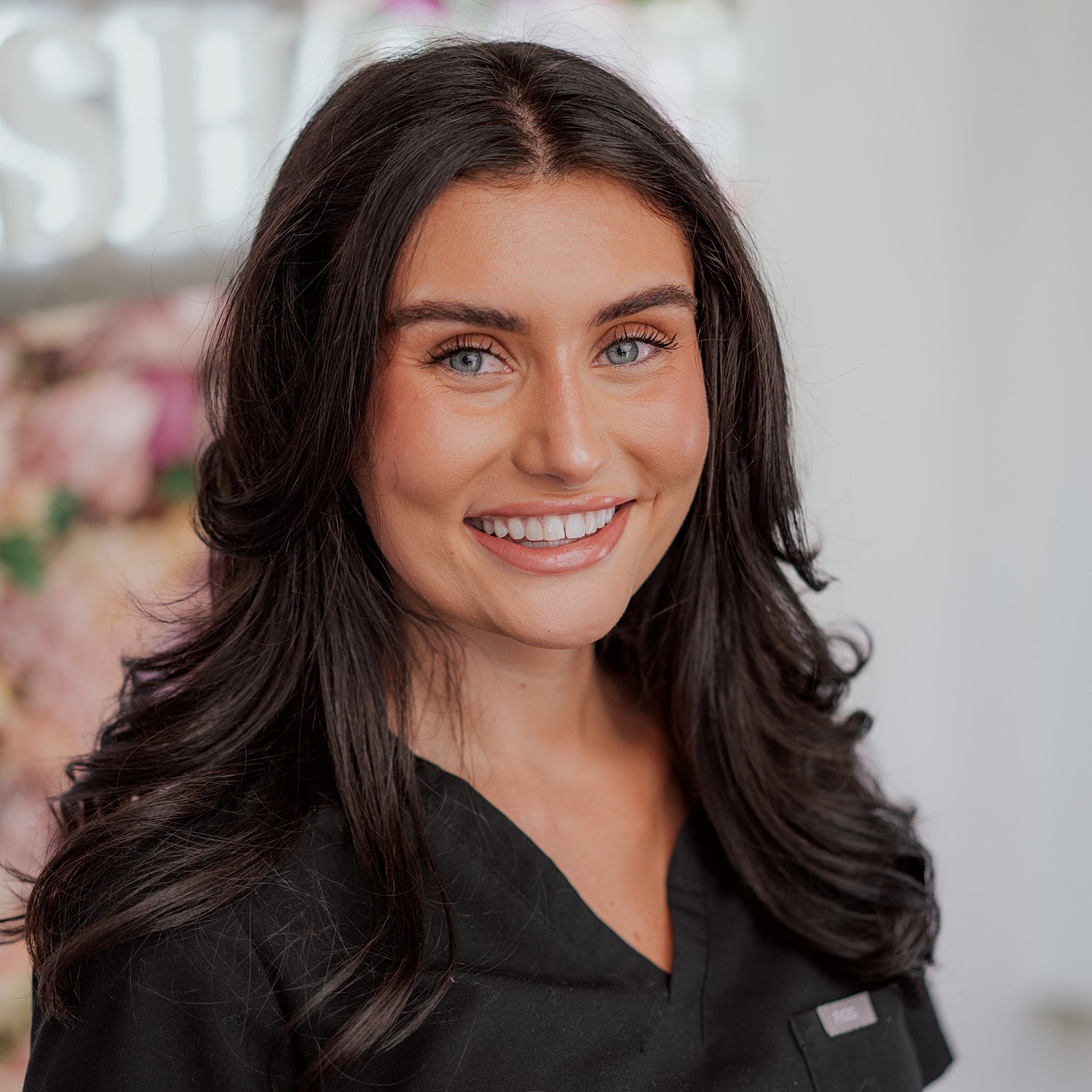 Smiling person in black uniform, floral background.