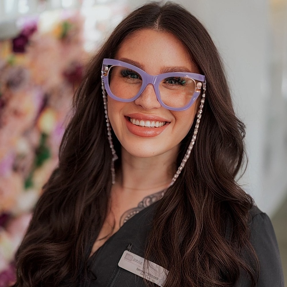 Smiling woman with purple glasses and long hair.