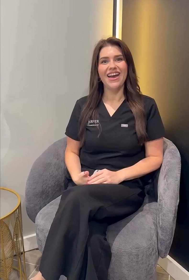 Smiling woman in medical attire sitting comfortably.