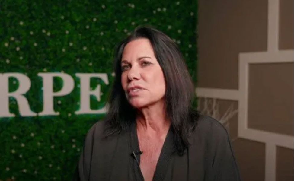 Person speaking in front of green backdrop.
