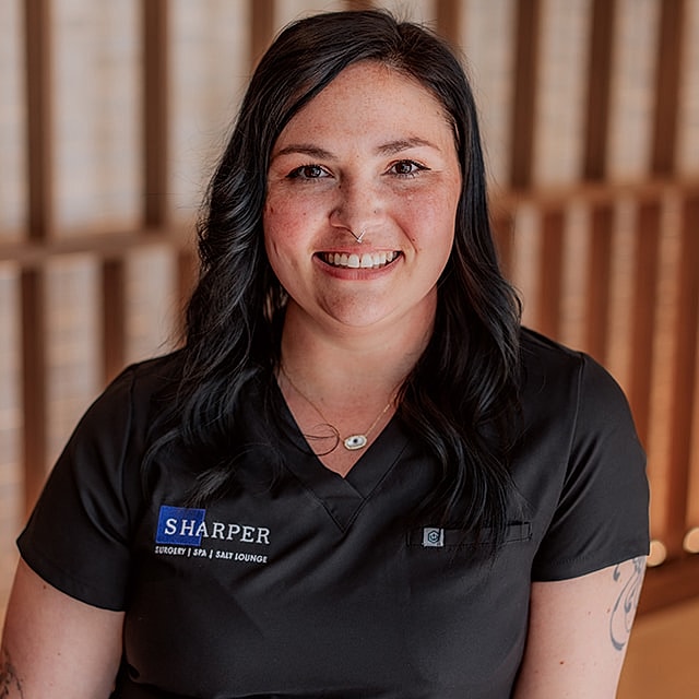 Smiling woman in medical attire against wooden background.