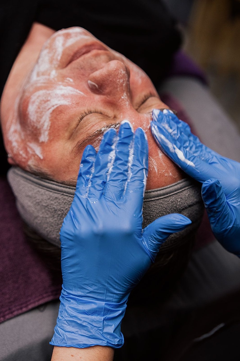 Facial treatment with gloved hands applying product.