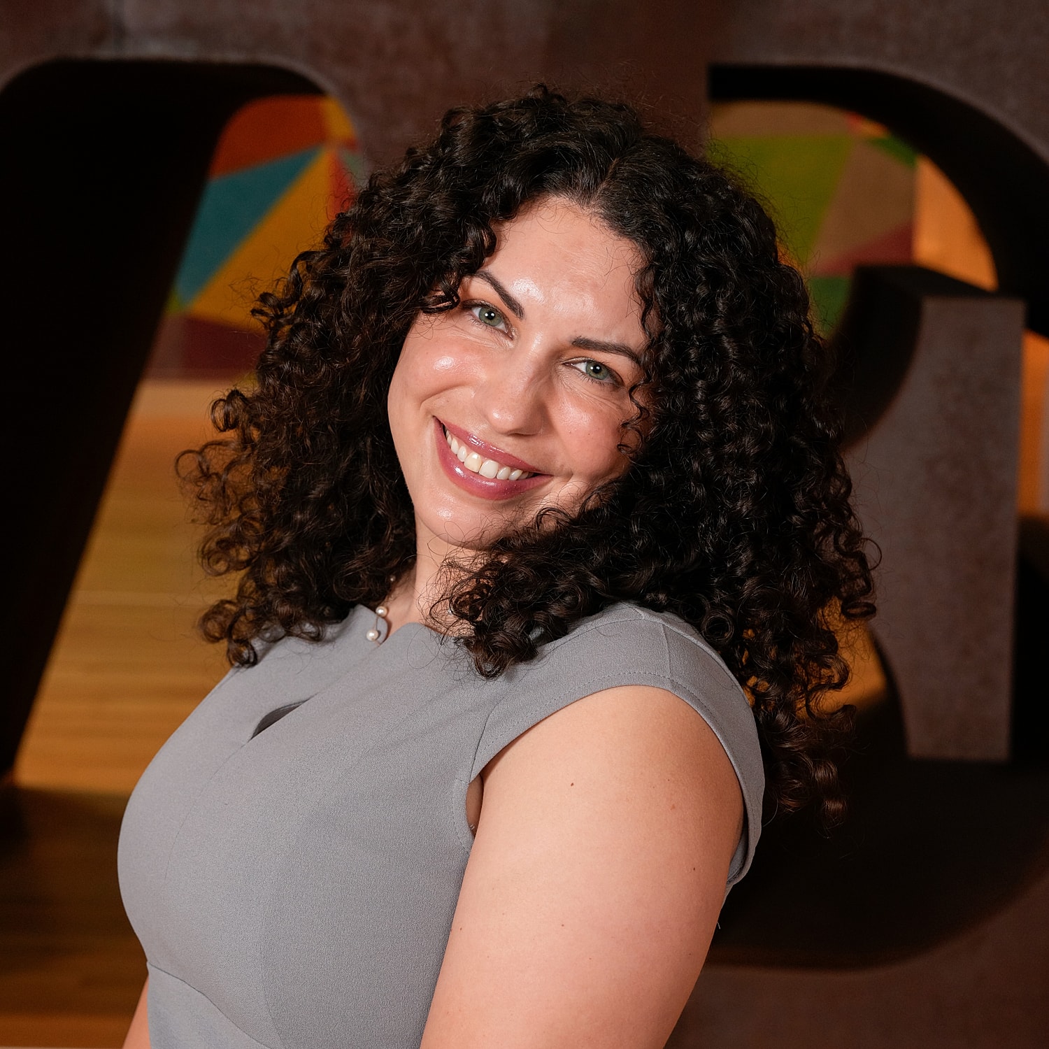 Smiling woman with curly hair in gray dress.