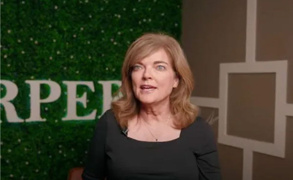 Woman speaking in front of greenery backdrop.